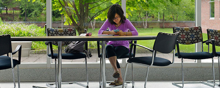 girl on her smart phone listening to music while studying at a table