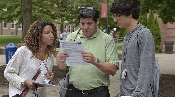 A student and his parents looking at forms and degree plans on orientation day.