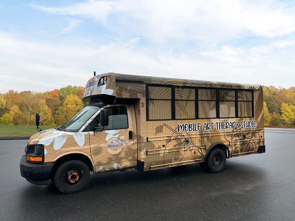 Exterior view of the Artlighten Mobile Art Therapy Studio bus parked outdoors, branded as a mobile space for art therapy services.