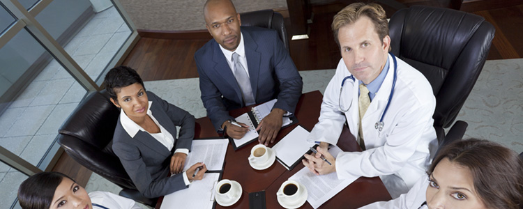Stock photo of a medical professional looking up with 2 other executives over a table.