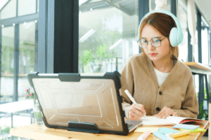 Woman writing in notebook while looking at a laptop screen