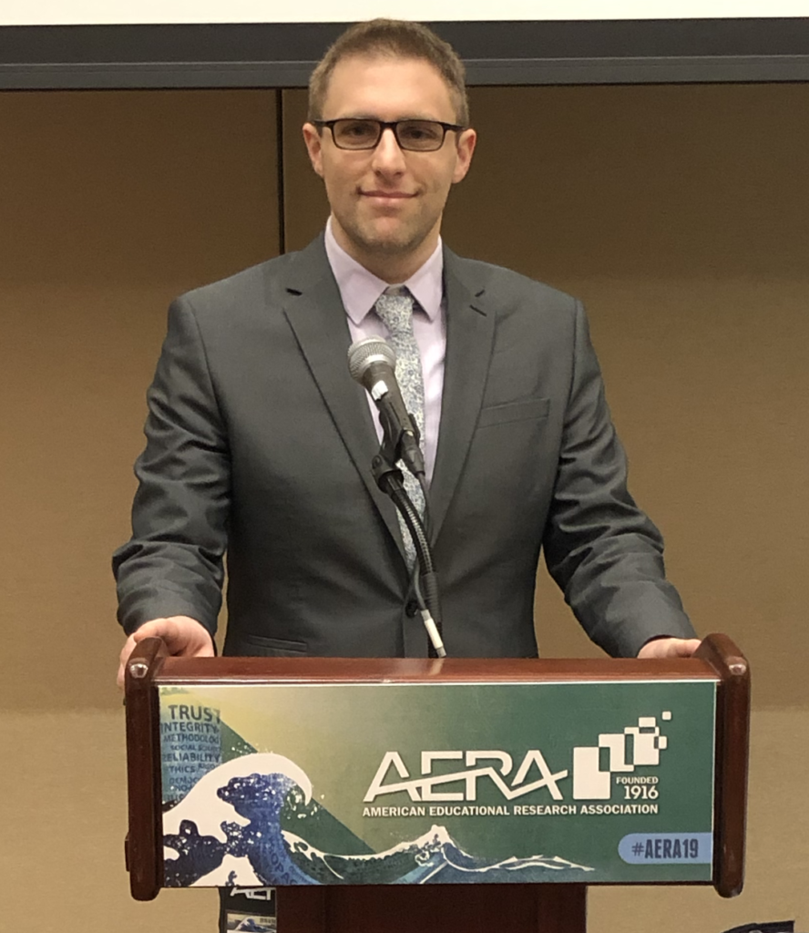 Dr. DeSantis standing in front of a podium at the AERA 2019 conference