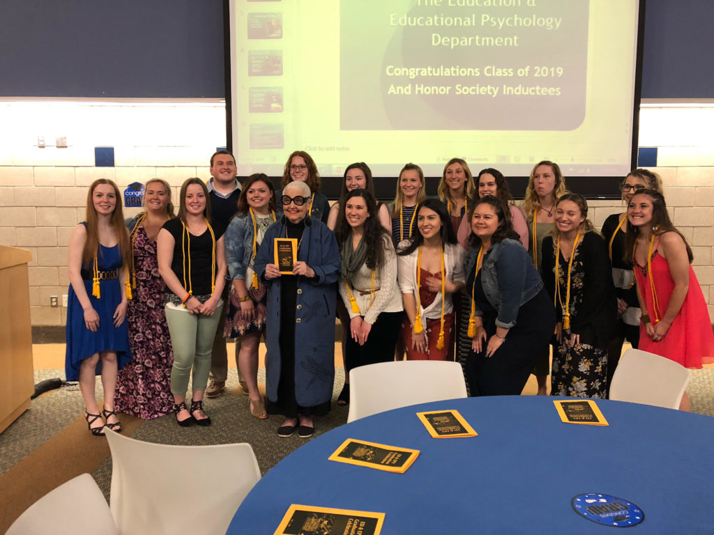 Class of 2019 and Honor Society Inductees standing at the front of the room wearing their gold cords
