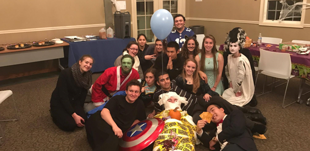 Many students wearing various Halloween costumes take a group photo. They include a mummy, the Wife of Frankenstein&#039;s Monster, and Walmart Captain America and the Hulk.