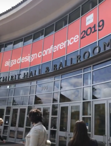The Pasadena Conference Center has a banner at the top that reads &quot;aiga design conference 2019&quot; in all lowercase white font (except 2019 is black). The front of the building is made up of many windows.