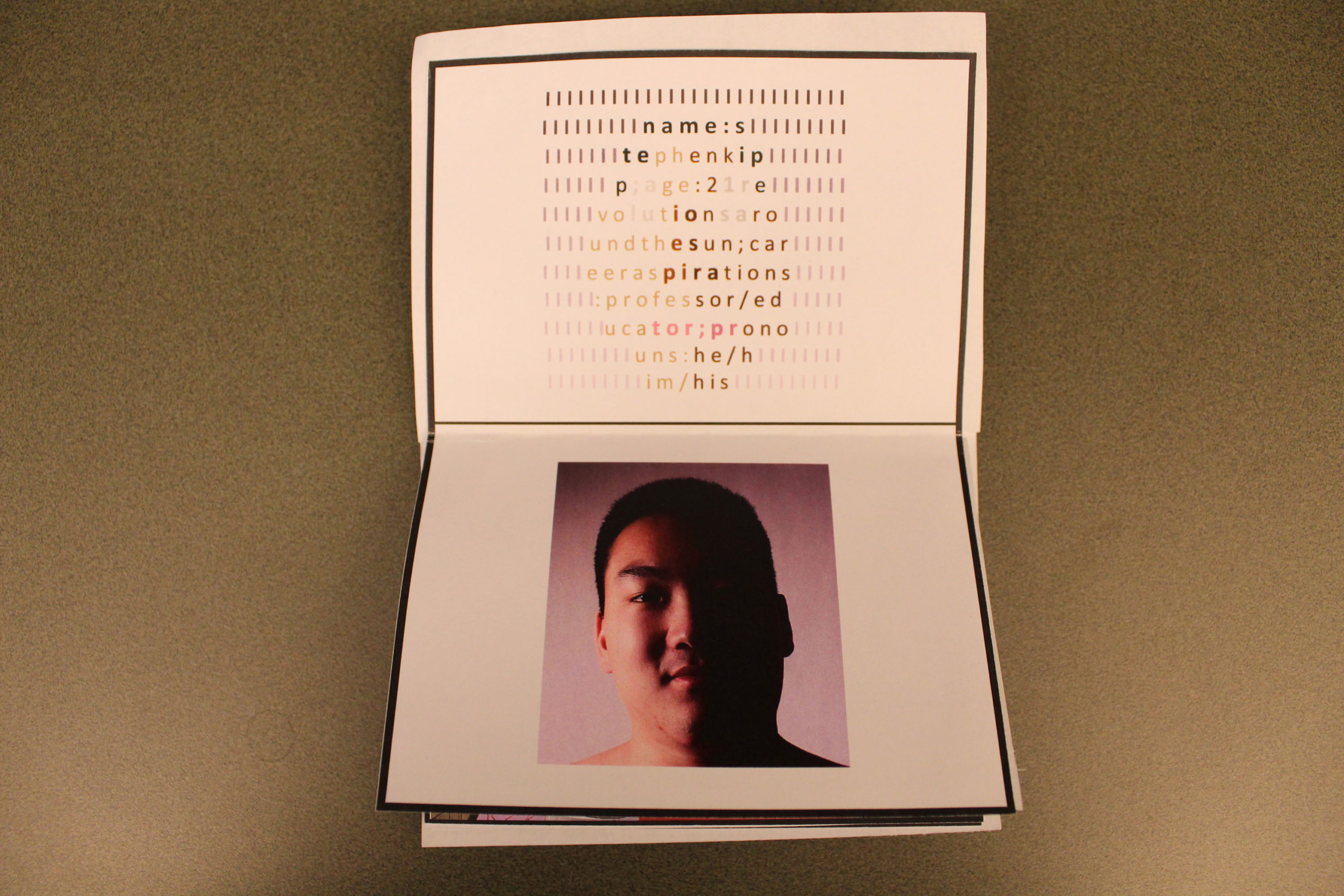 A folded piece of printer paper with black borders near the edges to create a passport. On the top is text that reads, "name: stephen kipp; age: 21 revolutions around the sun; career aspirations: professor/educator; pronouns: he/him/his." The text is wrapped in the shape of a face and is colored like a face. The face is surrounded by black lines that fade as they go down the page. On the bottom half is a picture of Stephen Kipp's face. They are male-presenting, and the right half of their face is dark.