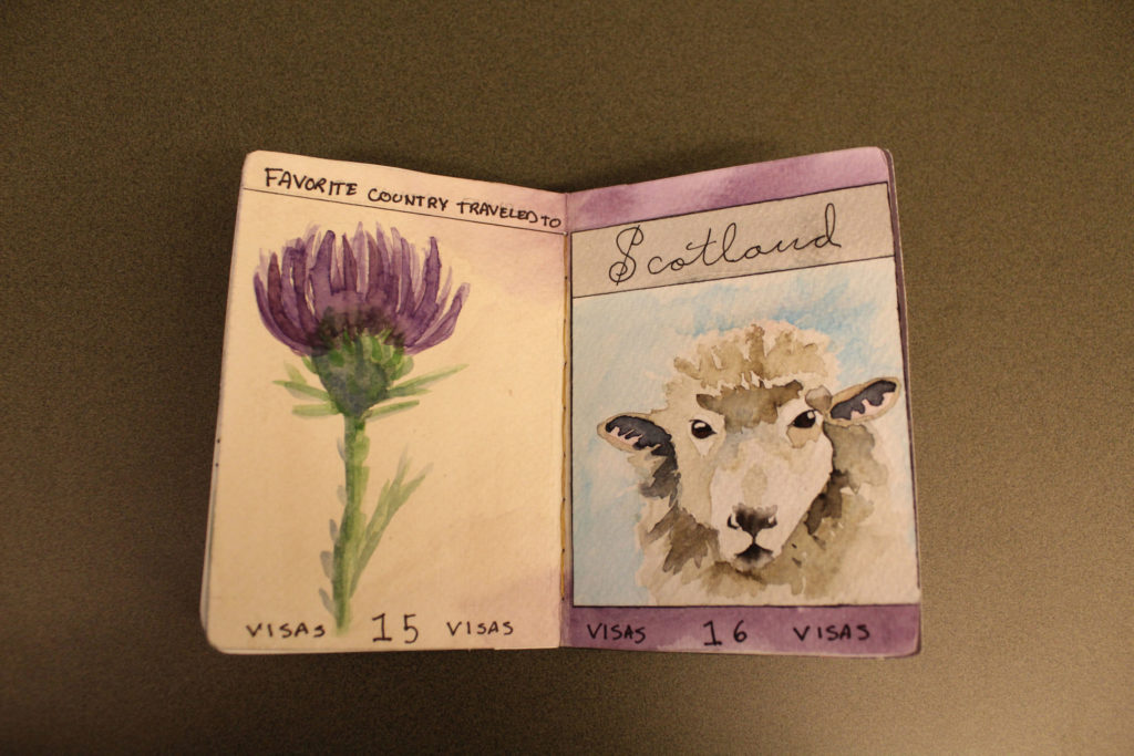 The left page of the passport has, "Favorite country traveled to," written at the top. The bottom says, "Visas 15 Visas." A purple thistle is painted on the page. "Scotland" is written in cursive on the top of the page, and "Visas 16 Visas" is written at the bottom. A sheep's face is painted against a light blue background in the middle of the page.
