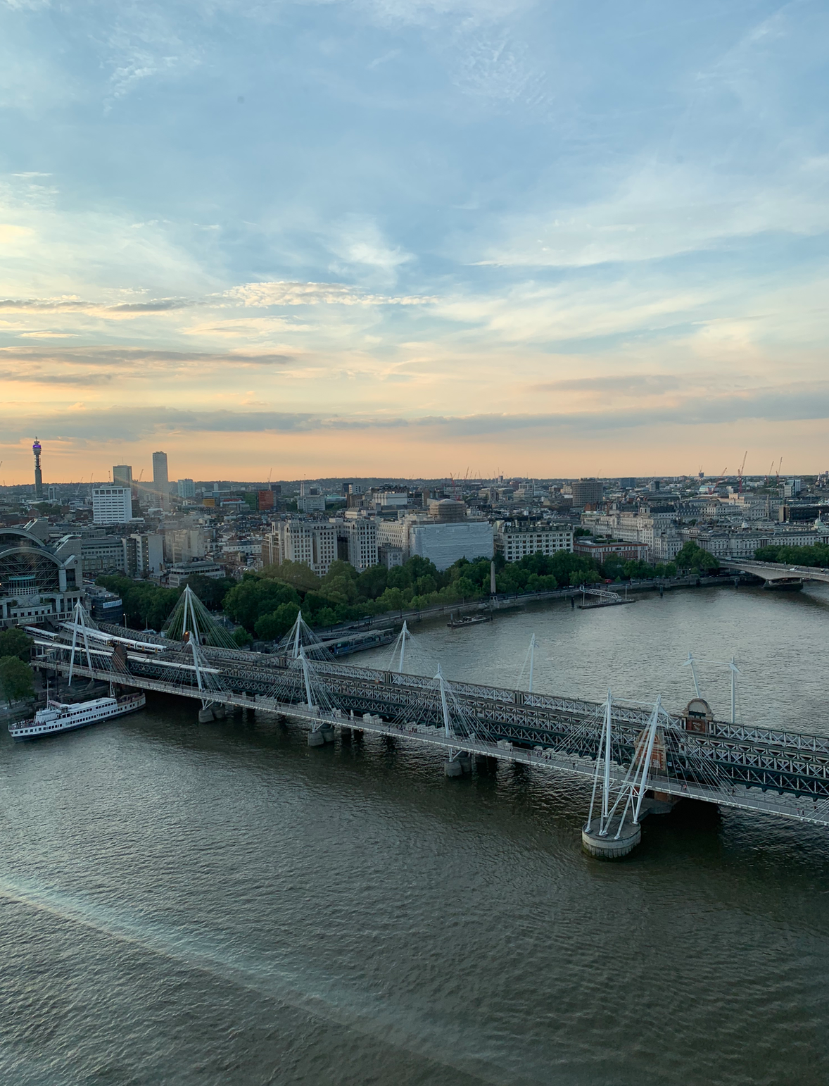 The Hungerford/Charing Cross bridge going over the River Thames. It is primarily cable-stayed with white wires and has train tracks going over it.