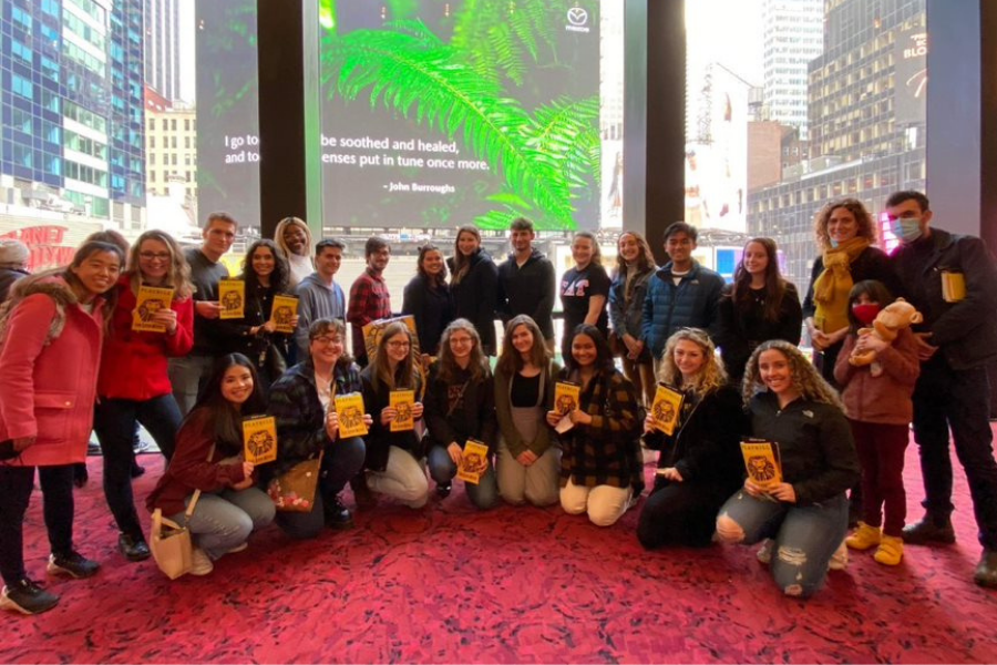 Students and honors staff standing in two half circles, one larger group standing and a smaller group kneeling. Most students hold up yellow Lion King Playbills.