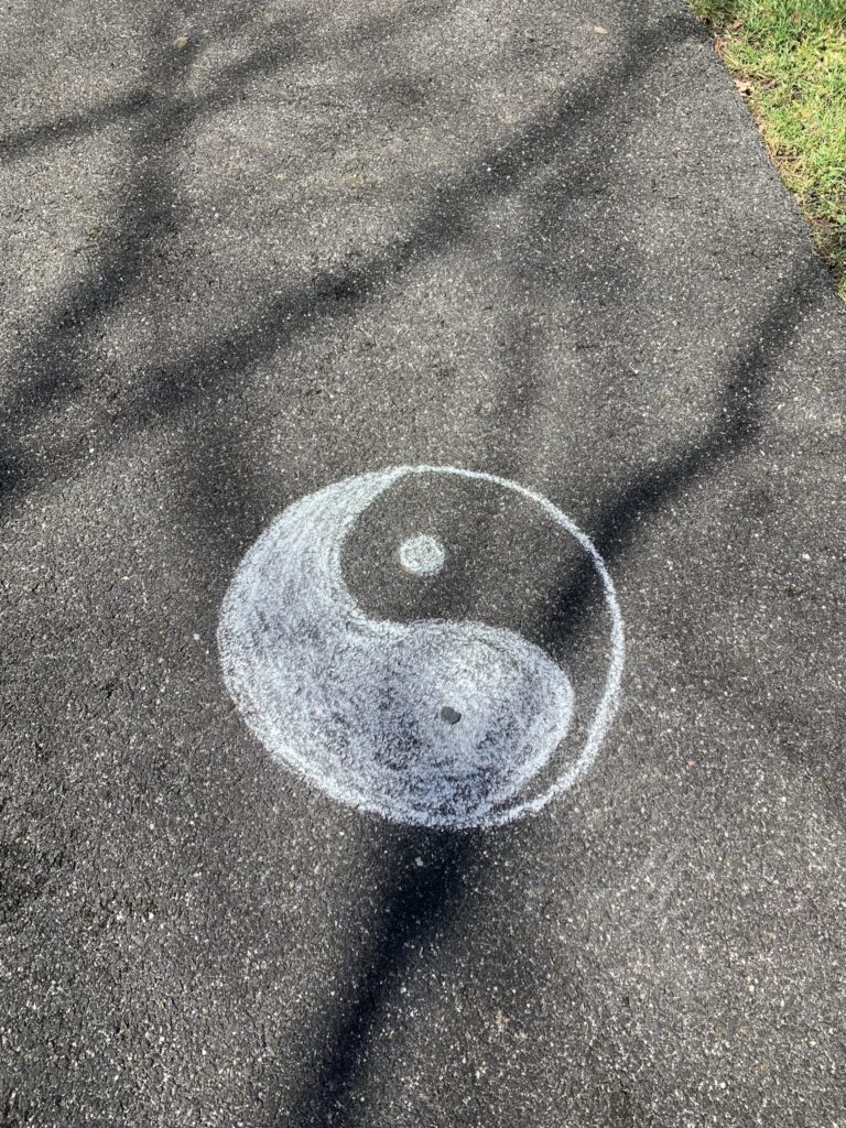 A yin-yang symbol, a Taoist image, drawn with chalk on dark pavement.