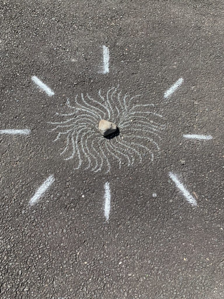 A rock is in the center of many squiggly chalk lines all forming a circle. Eight short, thick emphasis lines drawn outward are outside the squiggly lines.