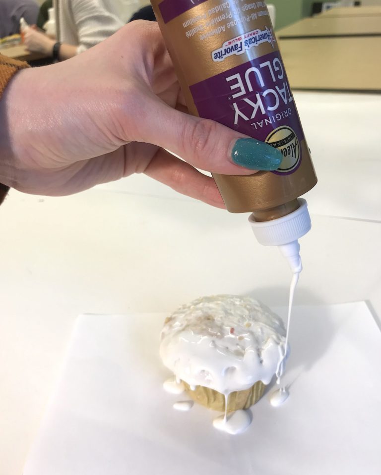A hand squeezes tacky glue on top of an inedible cupcake.