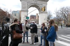 Students stand outside at a street corner. The arch in Washington Square Park stands behind them.