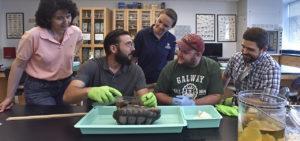 image of :  WCSU Professor of Biological and Environmental Sciences Dr. Theodora Pinou (pink shirt) observes a terrapin tracking team “train the trainer” session where Biology graduate student (l-r) Adam Geriak shares his sampling expertise with undergraduate Biology students James Hannon and Christopher Schrull. Bridget Cerevero, Education Manager of Citizen Science at the Maritime Aquarium (dark blue shirt), helps coach students on how to work with volunteers. 