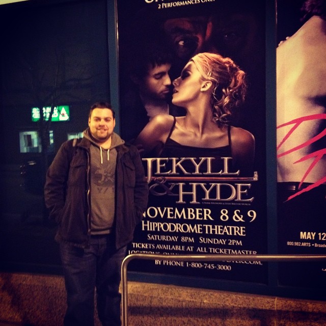 Image of Andrew Hendrick with "Jekyll & Hyde" poster outside theatre.